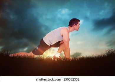 Side view of a young man in ready to run posture against blue sky over grass