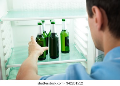 Side View Of Young Man Removing Beer Bottle From Refrigerator At Home