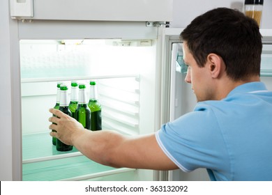 Side View Of Young Man Removing Beer Bottle From Refrigerator At Home