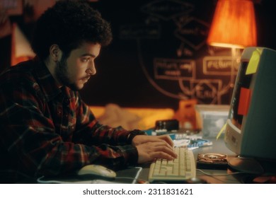 Side view of young man typing codes on keyboard on computer to develop new software