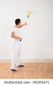 Side View Of Young Man Using Paint Roller On White Wall At Home