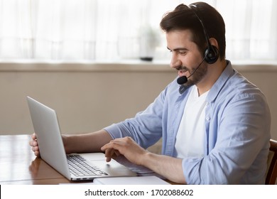 Side View Young Man Wearing Wireless Headset With Microphone, Looking At Laptop Screen, Study On Online Courses. Skilled Male Teacher Giving Online Educational Class To Client, Working Remotely.