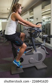 Side View Of A Young Man Working Out On Exercise Bike At The Gym