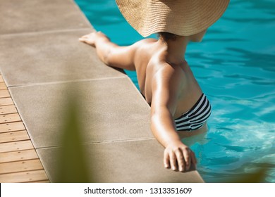 Side View Of Young Mixed Race Woman With Hat Leaning On Edge Of Pool In Backyard Of Her Home