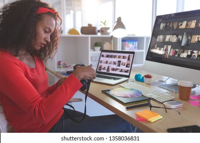 Side view of young mixed-race female graphic designer reviewing photos in digital camera at desk in a modern office - Powered by Shutterstock