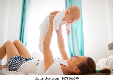 Side View Of Young Mother Lifting Baby Boy Above Her