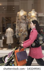 Side View Of Young Mother Pushing Baby Stroller By Clothes Shop