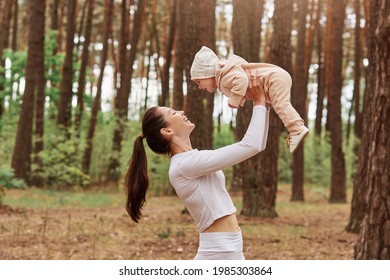 Side View Of Young Mother Throws Up Baby In Air While Happy Family Playing Together In Forest, Mom And Little Daughter, Positive Human Emotions, Feelings, Joy.