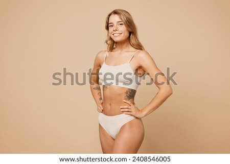 Side view young nice lady woman with slim body perfect skin wear nude top bra lingerie stand hold hands on waist look camera isolated on plain pastel light beige background. Lifestyle diet fit concept