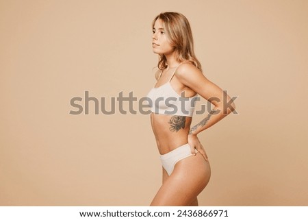 Side view young nice lady woman with slim body perfect skin wear nude top bra lingerie stand akimbo hold hand on waist back isolated on plain pastel light beige background. Lifestyle diet fit concept