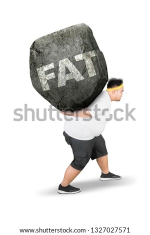 Side view of young obese man carrying fat word in a rock while walking in the studio