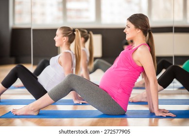 Side view of young pregnant women are doing exercise at gym.