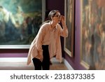 Side view of young pretty Caucasian woman carefully looking at picture. Masterpieces in background. Concept of the Museum Day.