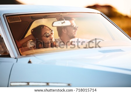 Side view of Young pretty couple sitting in car on sunset