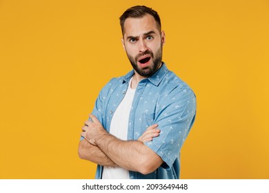 Side view young questioned indignant frowning caucasian man 20s wearing blue shirt white t-shirt hold hands crossed folded isolated on plain yellow background studio portrait. People lifestyle concept