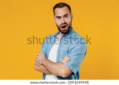 Side view young questioned indignant frowning caucasian man 20s wearing blue shirt white t-shirt hold hands crossed folded isolated on plain yellow background studio portrait. People lifestyle concept