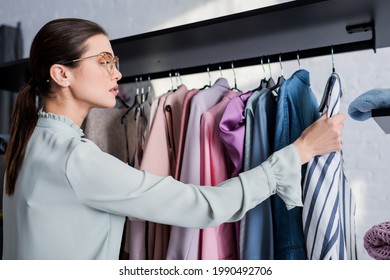 Side View Of Young Seamstress Looking At Clothes On Hanger