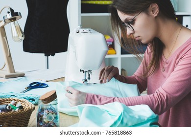 side view of young seamstress using sewing machine at workplace