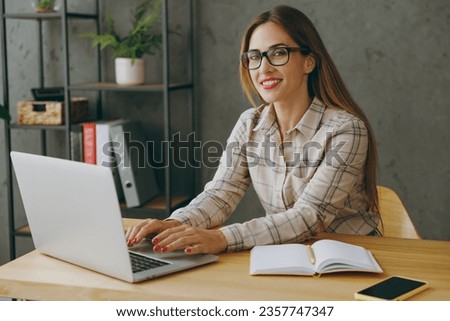 Side view young smart succesful employee business woman wearing shirt casual clothes glasses sit work at office desk with pc laptop computer notebook search information. Achievement career job concept