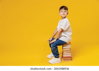 Side View Young Smart Wunderkind School Boy 5-6 Years Old In T-shirt Casual Clothes Sit On Pile Of Books Isolated On Plain Yellow Background Studio Childhood Children Kids Education Lifestyle Concept