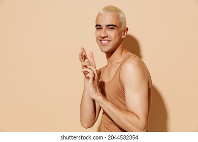 Side View Young Smiling Fun Blond Latin Hispanic Gay Man With Make Up In Beige Tank Shirt Hold Hands Look Camera Isolated On Plain Light Ocher Background Studio Portrait People Lgbt Lifestyle Concept