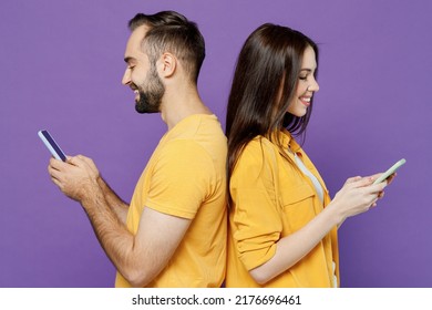 Side View Young Smiling Happy Cheerful Couple Two Friends Family Man Woman Together In Yellow Clothes Hold In Hand Use Mobile Cell Phone Stand Back To Back Isolated On Plain Violet Background Studio