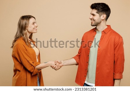 Side view young smiling happy couple two friends family man woman wear casual clothes looking to each other shaking hands together isolated on pastel plain light beige color background studio portrait