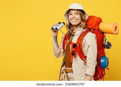 Side view young smiling woman carry backpack with stuff mat using binocular isolated on plain yellow background. Tourist leads active lifestyle walk on spare time. Hiking trek rest travel trip concept - Powered by Shutterstock