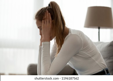 Side view young stressed depressed woman sitting on couch at home holding head with hands. Girl suffering from pain heartbreak after quarrel or break up with beloved one. Bad news big problems concept - Shutterstock ID 1196187562