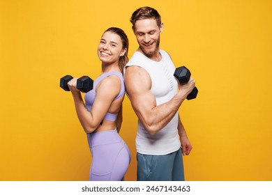 Side view young strong fitness trainer instructor sporty two man woman wear blue clothes spend time in home gym hold in hand dumbbells isolated on plain yellow background. Workout sport fit concept - Powered by Shutterstock