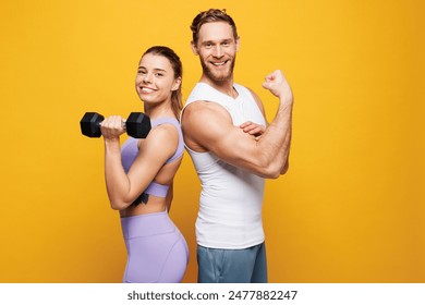 Side view young strong fitness trainer instructor sporty two man woman wearing blue clothes spend time in home gym hold in hand dumbbells isolated on plain yellow background. Workout sport fit concept - Powered by Shutterstock