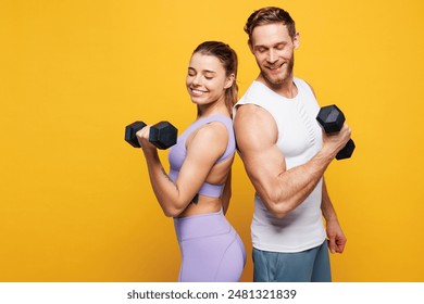 Side view young strong fitness trainer instructor sporty two man woman wear blue clothes spend time in home gym hold in hand dumbbells isolated on plain yellow background. Workout sport fit concept - Powered by Shutterstock