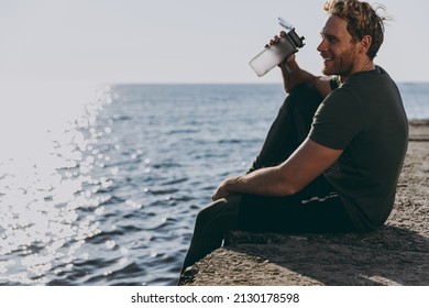 Side view young strong sporty toned fit sportsman man 20s wear sports clothes warm up training sit on pier hold bottle drink water at sunrise sun over sea beach outdoor seaside in summer day morning - Powered by Shutterstock