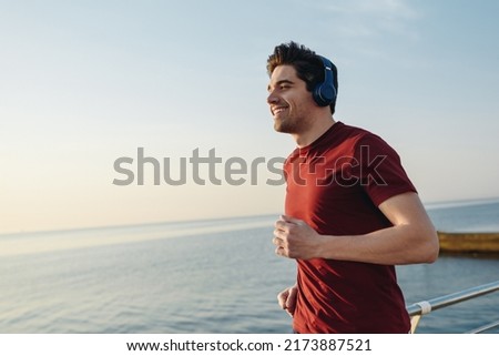 Side view young strong sporty athletic fit sportsman man wear sports clothes heapdhones listen music warm up training at sunrise sun dawn over sea beach outdoor on pier seaside in summer day morning