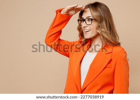 Side view young successful employee business woman corporate lawyer 30s wear formal orange suit glasses work in office hold hand at forehead look far away distance isolated on plain beige background