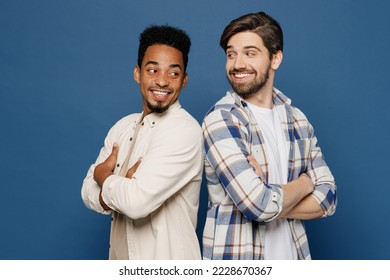 Side view young two friends happy cool men 20s wear white casual shirts together hold hands crossed folded look to each other isolated plain dark royal navy blue background. People lifestyle concept