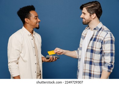 Side view young two friends happy fun men 20s wear white casual shirts together hold wireless modern bank payment terminal to process acquire credit card isolated plain dark royal navy blue background - Shutterstock ID 2249729307