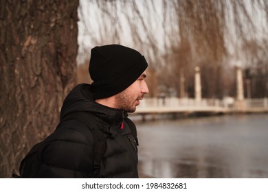 A Side View Of A Young Ukrainian Bearded Male Wearing A Black Beanie And A Winter Jacket In A Park