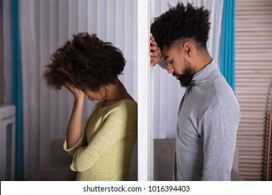 Side View Of Young Unhappy Couple Standing Back To Back At Home