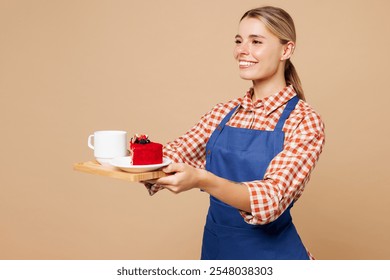 Side view young woman barista bartender barman employee wear blue apron red shirt work in coffee shop hold cake dessert order, tea cup isolated on plain beige background Small business startup concept - Powered by Shutterstock