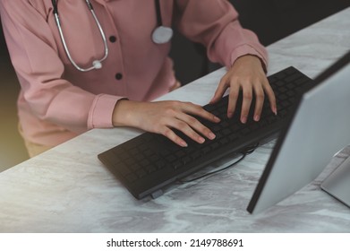 Side View Of A Young Woman Doctor Sitting Working On A Computer At Her Desk