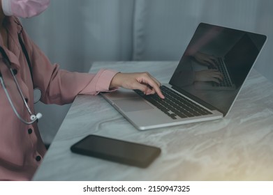 Side View Of A Young Woman Doctor Sitting Working On A Computer At Her Desk