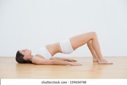Side view of young woman doing the bridge pose in fitness studio