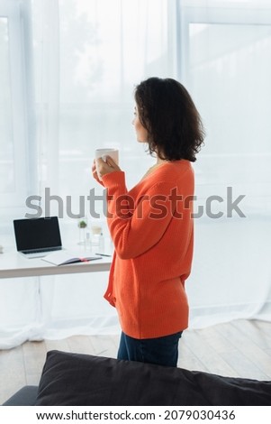 side view of young woman holding cup of coffee at home