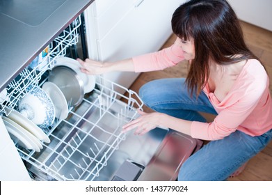 side view of young woman in kitchen doing housework. middle aged girl in the kitchen using dishwasher