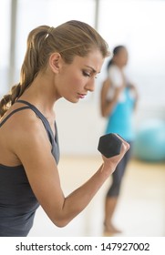 Side View Of Young Woman Lifting Dumbbell At Health Club