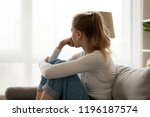 Side view young woman looking away at window sitting on couch at home. Frustrated confused female feels unhappy problem in personal life quarrel break up with boyfriend or unexpected pregnancy concept