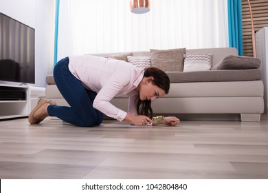 Side View Of A Young Woman Looking At Hardwood Floor Through Magnifying Glass