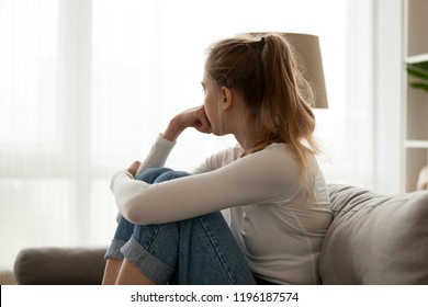 Side view young woman looking away at window sitting on couch at home. Frustrated confused female feels unhappy problem in personal life quarrel break up with boyfriend or unexpected pregnancy concept - Shutterstock ID 1196187574
