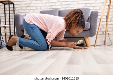 Side View Of A Young Woman Looking At Hardwood Floor Through Magnifying Glass